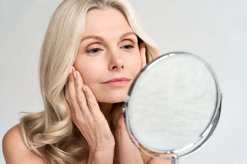 A woman checking her skin in a hand mirror